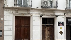 A building with two large wooden doors, a small outdoor seating area with tables and chairs, and a sign on the wall.