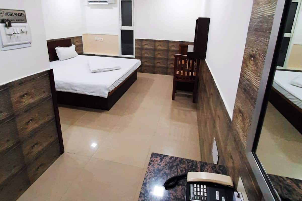 Habitación de hotel con cama, escritorio con teléfono, silla, espejo y aire acondicionado de pared.