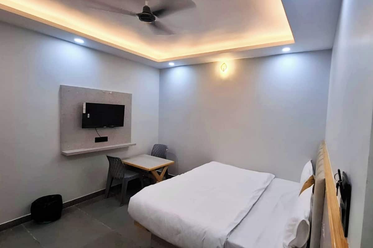 Habitación de hotel con cama, escritorio, silla, televisión instalada en la pared y ventilador de techo.