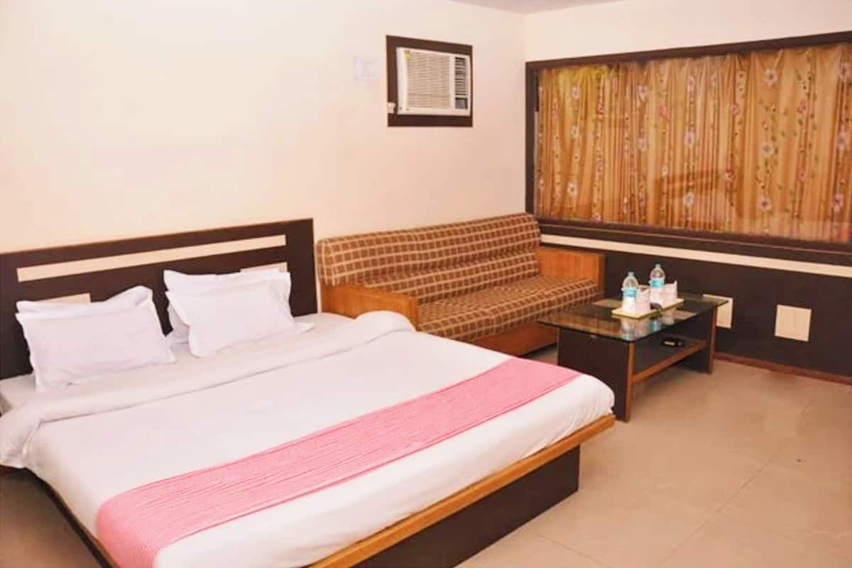 Habitación de hotel con cama, sofá, una mesita con artículos de aseo y una ventana con cortinas.