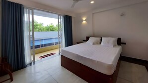 Une chambre d’hôtel avec un grand lit, un ventilateur de plafond et une vue sur une piscine, accessible par une porte-fenêtre coulissante.