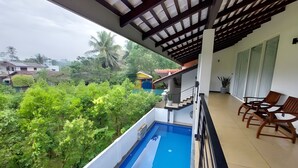 Un balcon avec une piscine, des chaises en bois et une vue sur la verdure et les bâtiments.