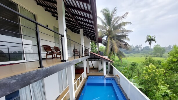 Un espace aménagé au bord de la piscine, offrant une vue sur un paysage verdoyant luxuriant, avec un coin salon abrité et une grande fenêtre donnant sur le paysage.