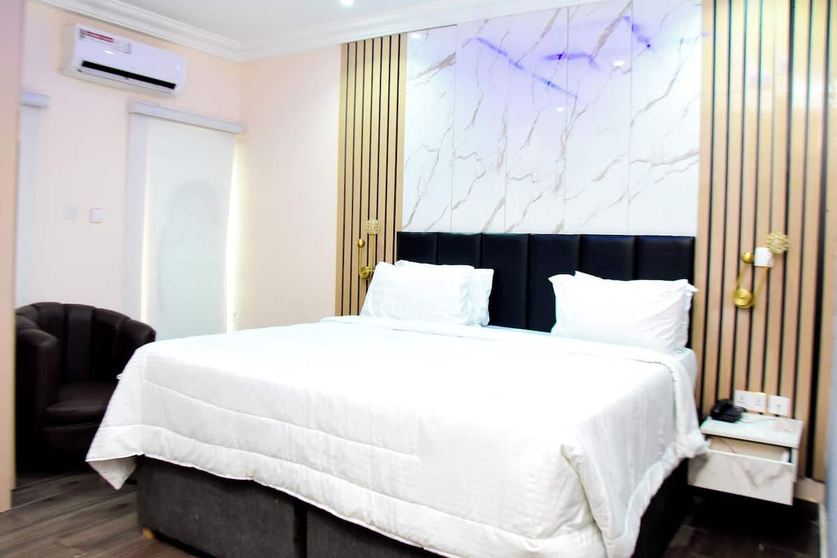 Une chambre d’hôtel avec un grand lit, une chaise, une table de chevet et un mur au motif évoquant le marbre.