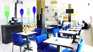 Ein Restaurantinneres mit blauen Stühlen, weißen Tischen, einer schwarzen Theke und einer modernen Pendelleuchte.