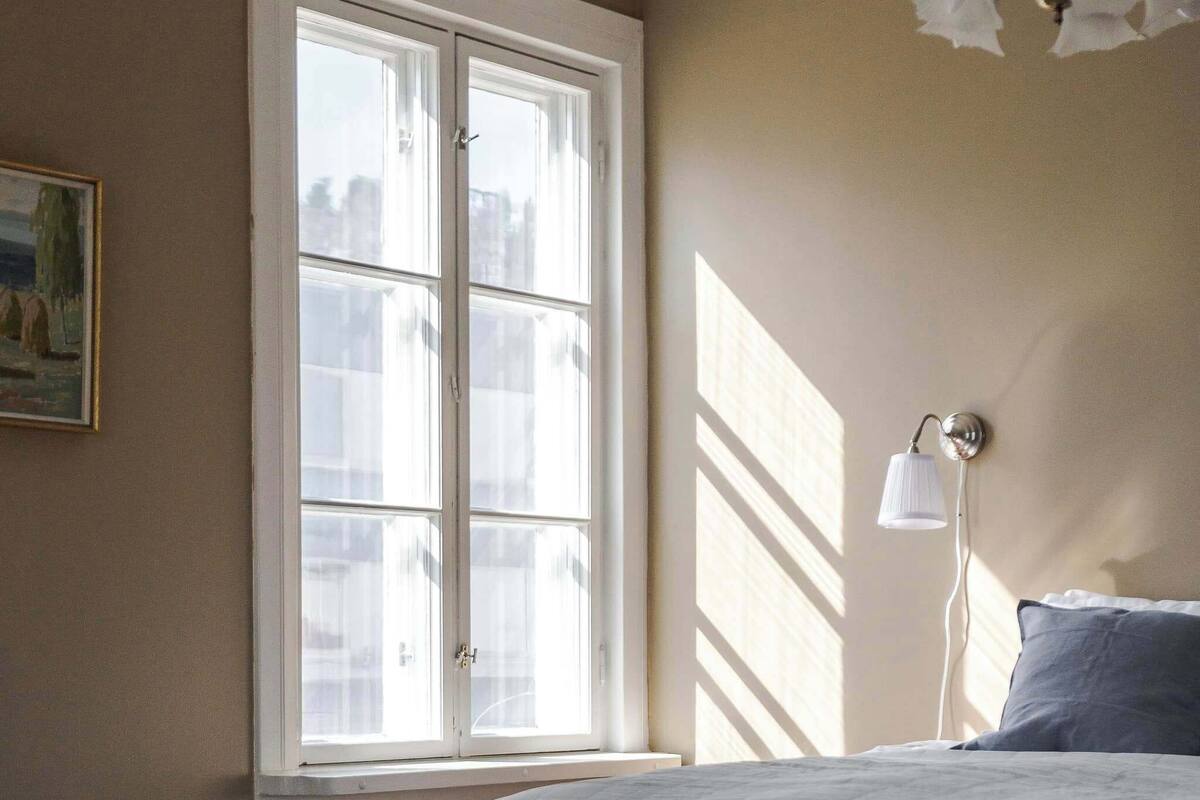 A bedroom with a large window, a bedside lamp, and a bed with a blue pillow.