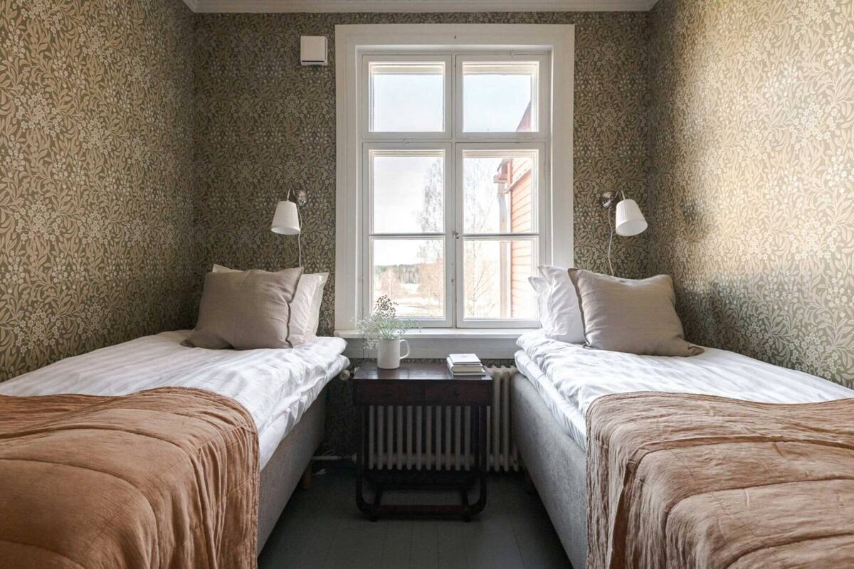 A bedroom with two single beds, a radiator, a window, and a small table with a plant.