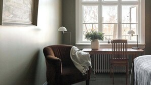 Et værelse med et stort vindue, en radiator, en stol, et bord og en seng.