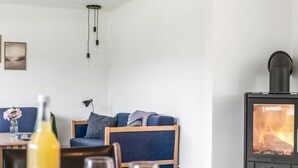 A cozy living room with a sofa, a table with glasses, a bottle, and a wood-burning stove.