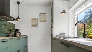 A modern kitchen with green cabinets, a coffee maker, and framed botanical charts on the wall.