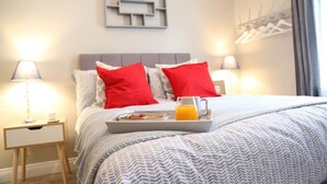 A neatly made bed with a tray of breakfast and a mug of orange juice, a bedside table with a lamp, and a wall-mounted coat rack. - Number 4 Old Tiverton Rd (Exeter)