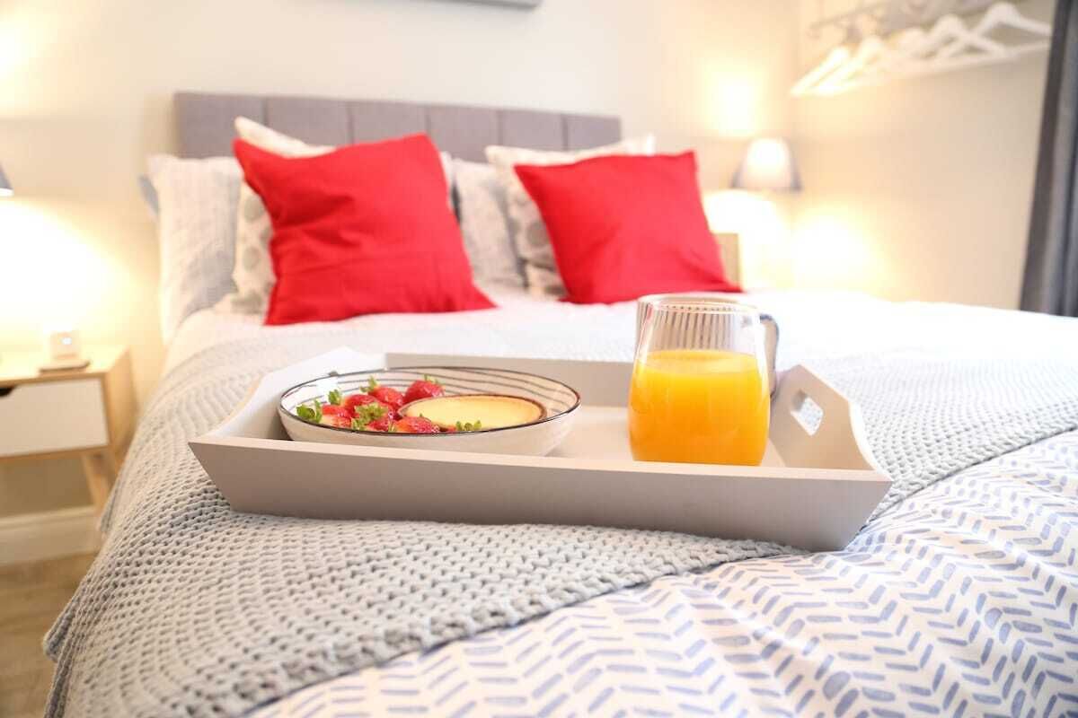 A neatly made breakfast tray with a bowl of cereal and a glass of orange juice on a bed with a grey and white patterned bedspread.