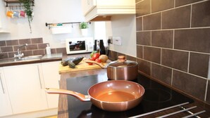A kitchen with an induction cooktop, a copper pan, and a cutting board with vegetables. - Number 4 Old Tiverton Rd (Exeter)