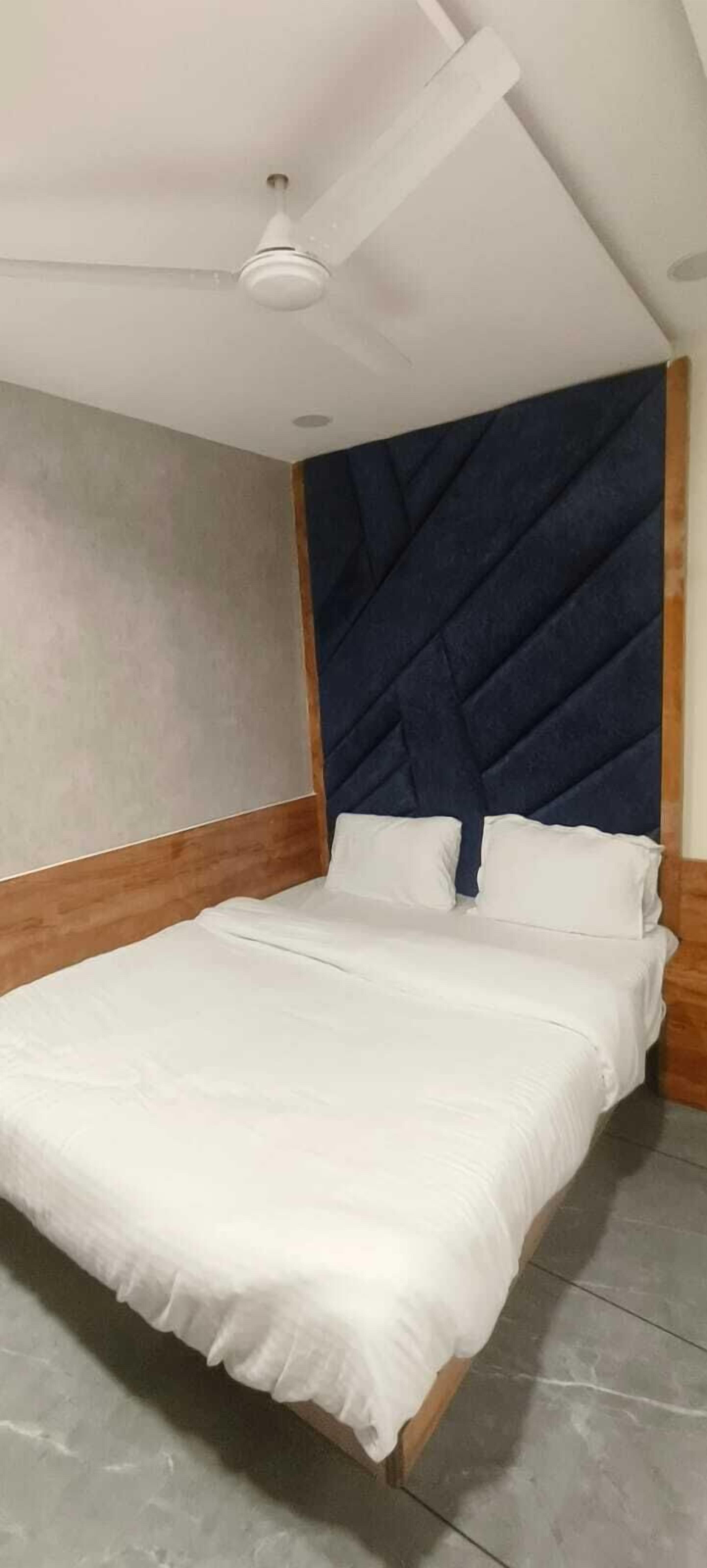 A bedroom with a bed, a ceiling fan, and a dark blue headboard.
