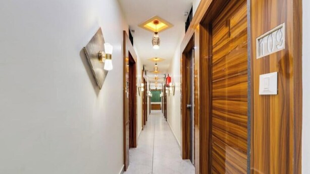 A hotel corridor with wooden doors, a tiled floor, and ceiling lights. - hotel shagun inn  (Ahmedabad)