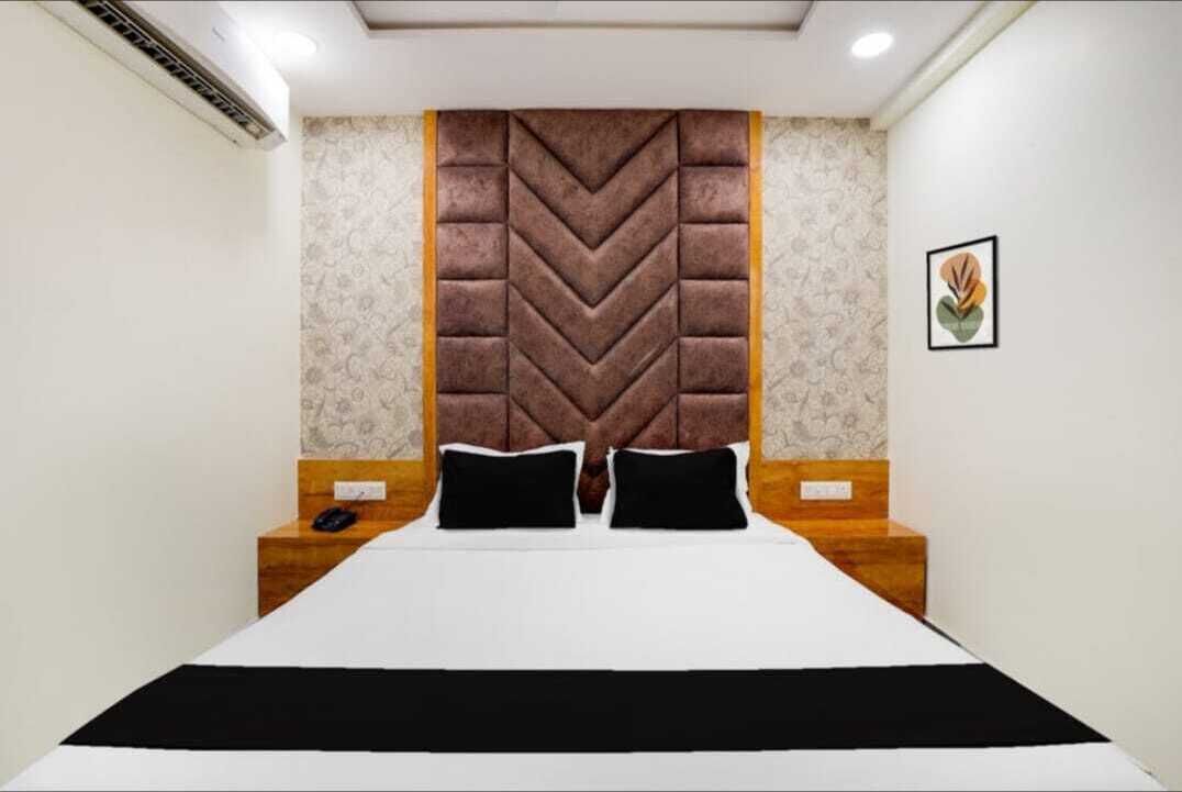 A hotel room with a large bed, a decorative headboard, a bedside table, and a framed picture on the wall.
