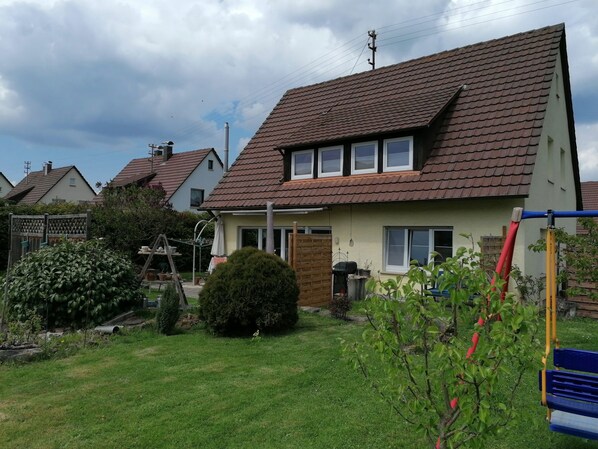 A residential house with a sloped roof, a fenced yard, and a swing set.