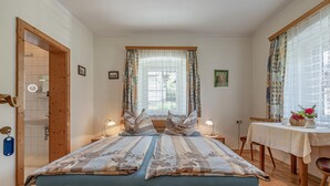 Un dormitorio con una cama de madera, una ventana con cortinas, una mesita de noche con lámpara y una pequeña mesa con un jarrón de flores.