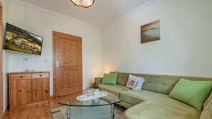 Una sala de estar con una mesa de centro de vidrio, un sofá, un mueble de madera, un televisor y un cuadro en la pared.