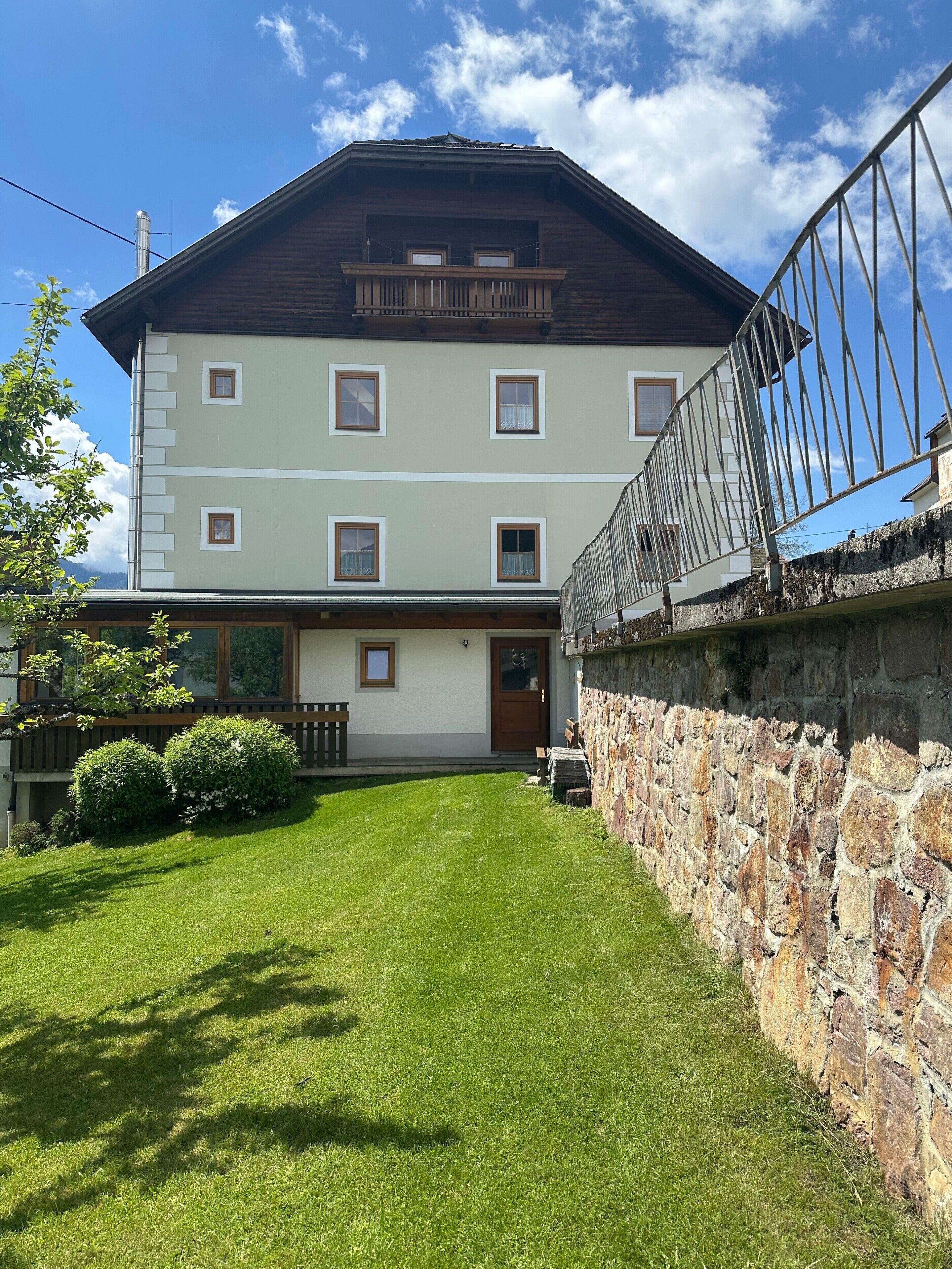 Ein mehrstöckiges Gebäude mit einer Steinmauer, einer Holzterrasse und einem Rasen.