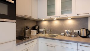 Una cocina moderna con armarios blancos, un lavamanos de acero inoxidable y una cafetera.