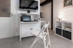 Cocina moderna con encimera blanca, una computadora portátil, un televisor sobre la encimera y una silla blanca en frente.