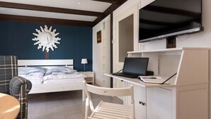 Un dormitorio con cama, escritorio con computadora portátil, televisor y decoración de pared con forma de sol.