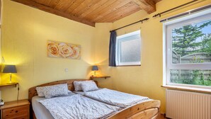 A bedroom with a wooden bed, two bedside tables with lamps, a window with a view, and a wall-mounted artwork.