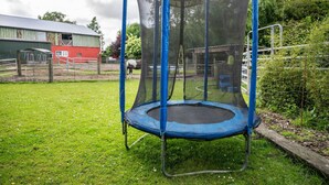 A trampoline with a safety net in an outdoor area with a red barn and a fenced enclosure in the background.