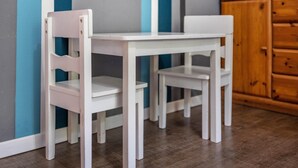 A white table and two white chairs in a room with a wooden cabinet and a wall with vertical stripes.