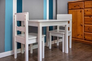 Une table blanche et deux chaises blanches se trouvent dans une pièce où il y a un meuble en bois et un mur orné de rayures verticales.