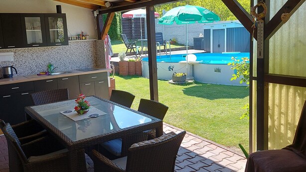 Een overdekt terras met een eettafel, stoelen en uitzicht op een zwembad.