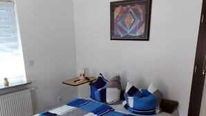 Een slaapkamer met een bed, kussens, een nachtkastje, een ingelijste foto en een raam.