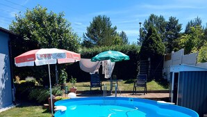 Een rond bovengronds zwembad met een blauw interieur, omgeven door gras, met twee parasols en een stoel op de achtergrond.