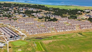 Ett bostadsområde vid kusten med flera husrader, en golfbana och en stor vattenyta i bakgrunden.