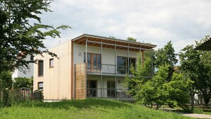 Ein modernes, zweistöckiges Gebäude mit Holzfassade, großen Fenstern und einem Balkon.