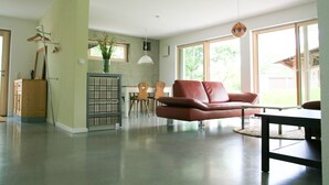 Ein geräumiges Wohnzimmer mit einem roten Sofa, einem Essbereich und großen Fenstern.