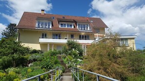 A two-story building with a red-tiled roof, a balcony with white railings, and a staircase leading to the entrance. - Apartment 2 with Terrace (Stetten)