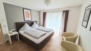 A modern bedroom with a large bed, a bedside table, a chair, and a window with curtains. - Apartment 2 with Terrace (Stetten)