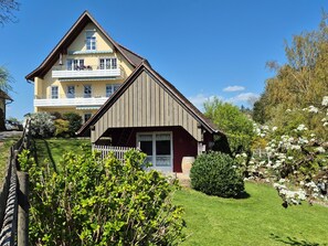 A two-story house with a sloped roof, a balcony, and a well-maintained garden.