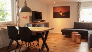 A modern living room with a dining area, a sofa, a TV, and a painting on the wall.