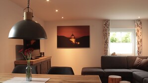 A modern living room with a wooden dining table, a sofa, and a painting on the wall.