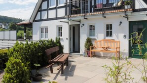 A two-story house with a balcony, a wooden bench, and potted plants.