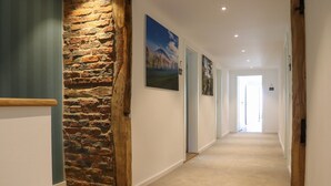 A hallway with a stone wall, a carpeted floor, and framed pictures on the wall.