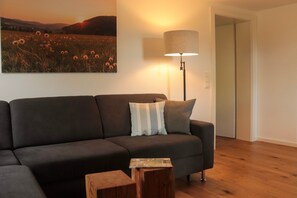 Ein modernes Wohnzimmer mit einer dunklen Couch, einer Lampe, einem Holztisch und einem Gemälde von einem Feld.