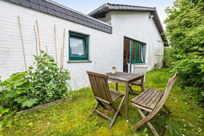 En hvid bygning med grønne vinduer og et træbord med stole i gården.
