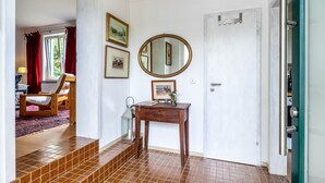 A room with a wooden chair, a small table with a mirror, and a door with a green frame.