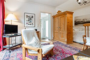 A room with a wooden chair, a television on a stand, a cabinet, and a patterned rug. - Apartment 'Im Reiterparadies' with Private Terrace, Private Garden and Wi-Fi (Salzhausen)