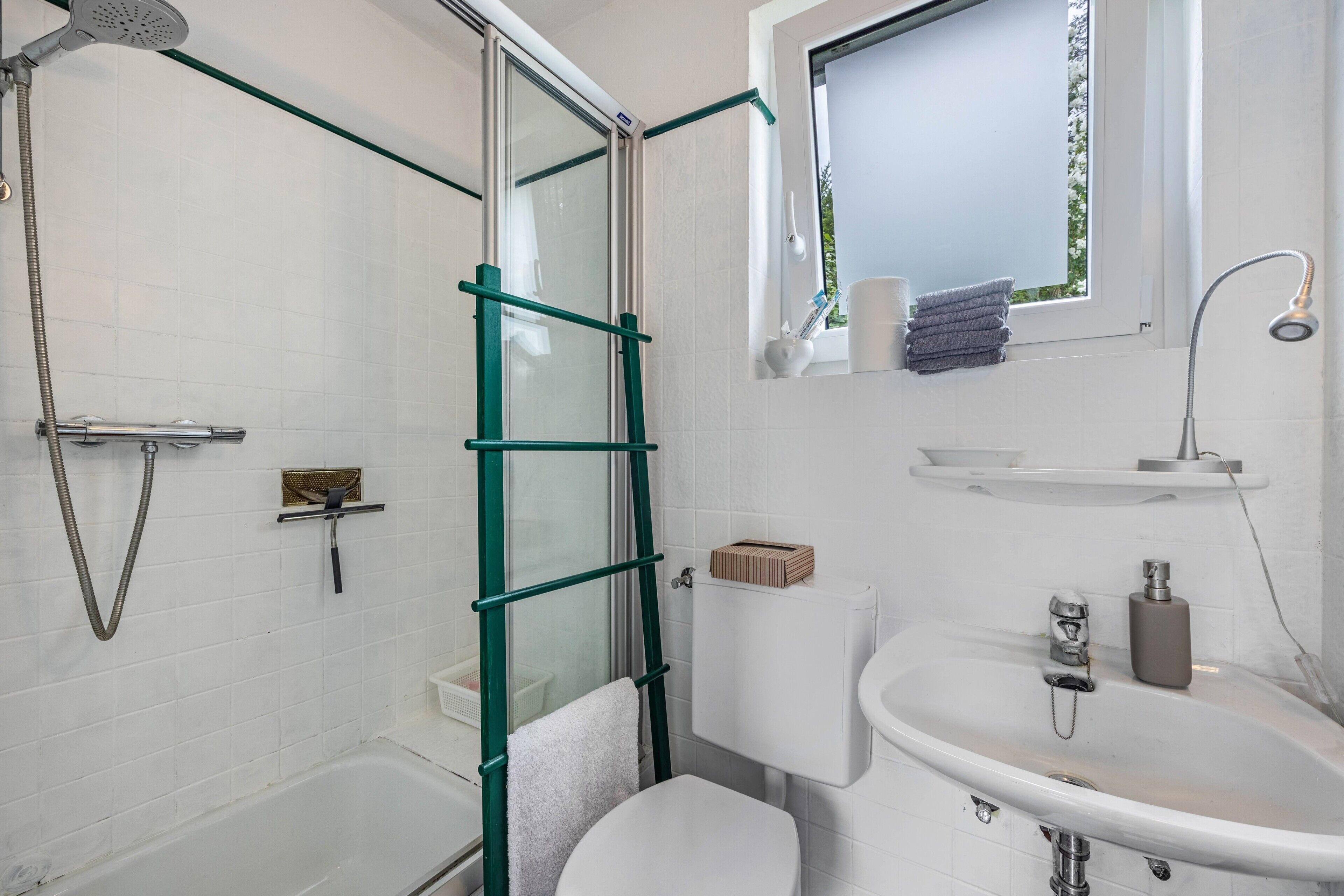 A bathroom with a glass shower enclosure, a white toilet, a sink with a mirror, and a window above the sink.