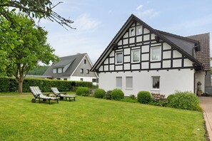Une maison traditionnelle à colombages, dotée d’une pelouse bien entretenue et de deux fauteuils de jardin.